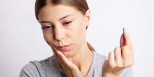 Person at home holding their cheek with severe tooth pain, deciding whether it can wait
